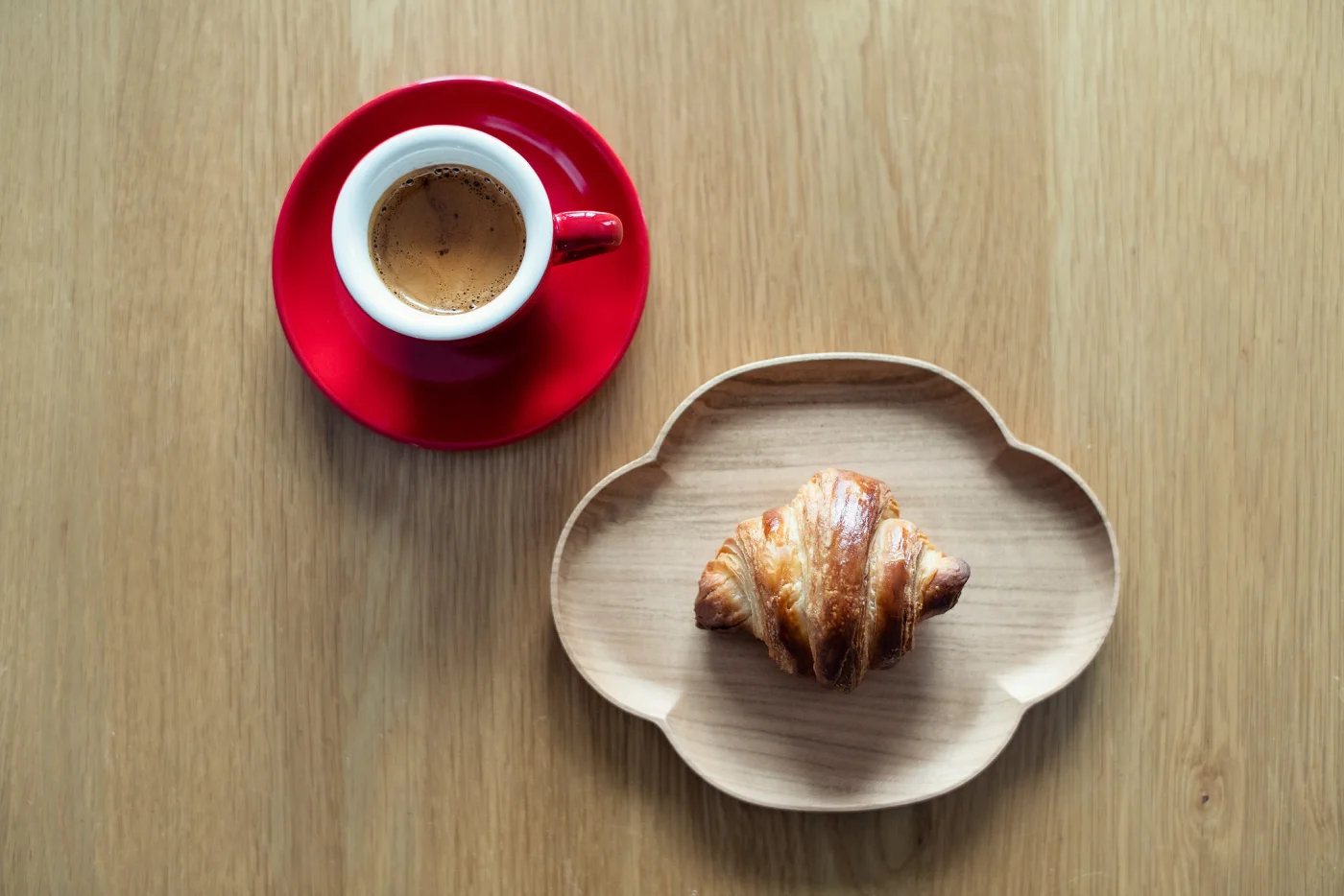 A red espresso cup and croissant on a wooden table