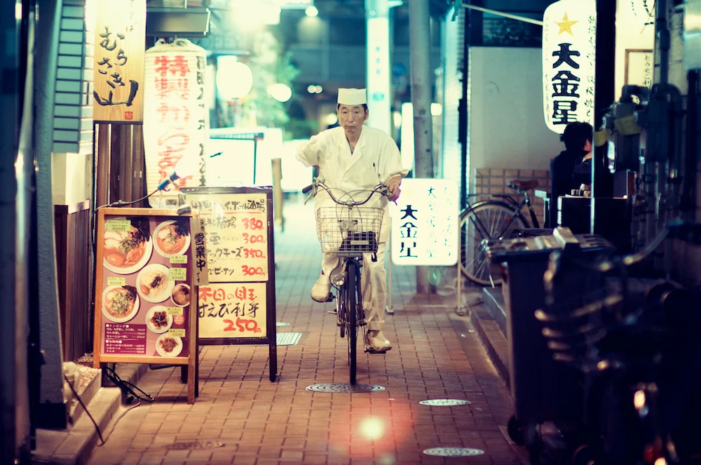Sushi delivery rider cycling down a glowing Japanese street